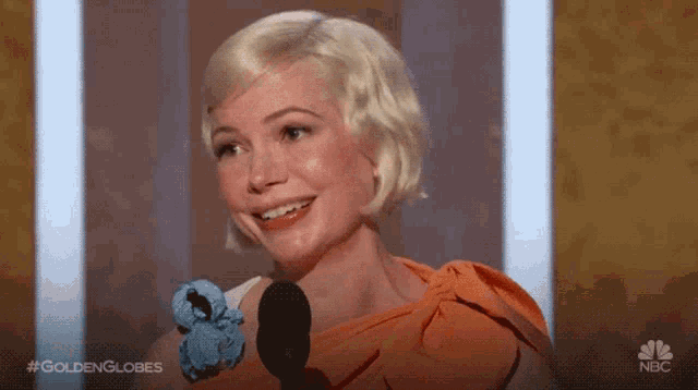 a woman is smiling in front of a microphone at a golden globes event .