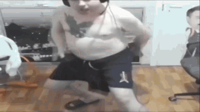 a man with a tattoo on his chest is dancing in a room while wearing shorts and headphones .