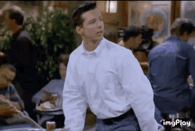 a man in a white shirt and blue pants is standing in front of a crowd of people in a restaurant .