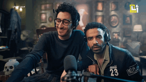 two men are sitting in front of a microphone and one of them has the number 23 on his jacket