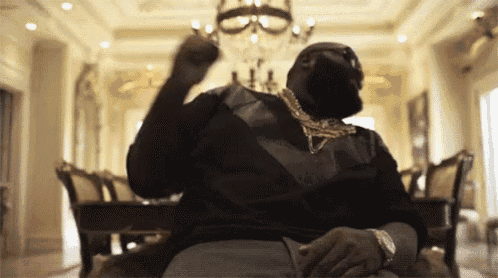 a man in a black shirt and gold chains is sitting in a room