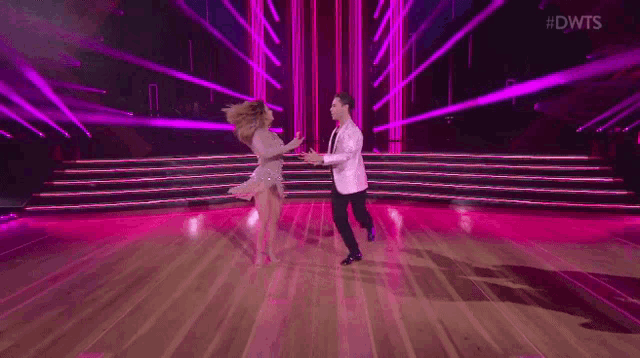 a man and a woman are dancing on a dance floor with purple lights behind them and the words #dwts on the bottom