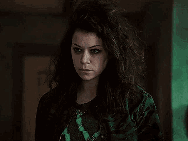 a woman with curly hair is wearing a green jacket and a green sweater .