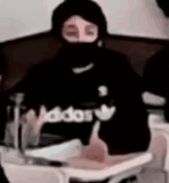 a person wearing a mask is sitting at a desk with a laptop .