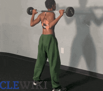 a woman is squatting with a barbell on her shoulders in front of a wall that has the word clewiki on it