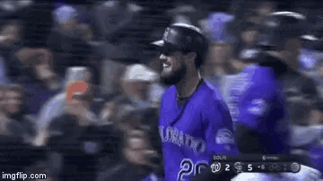 a baseball player wearing a purple uniform is standing in the dugout during a game .