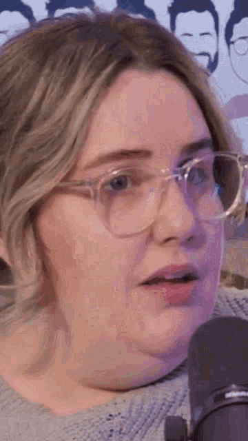a close up of a woman wearing glasses and a sweater talking into a microphone .