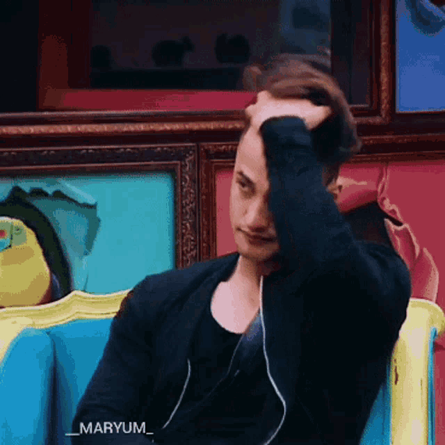 a man sitting on a couch with his hand on his head and the name maryum on the bottom right