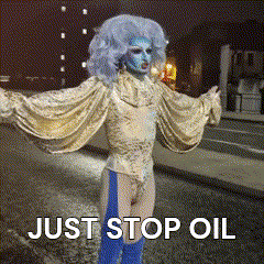 a drag queen with blue hair is standing on a street with the words just stop oil written on the bottom