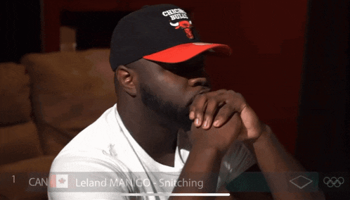 a man wearing a chicago bulls hat sits with his hands on his chin
