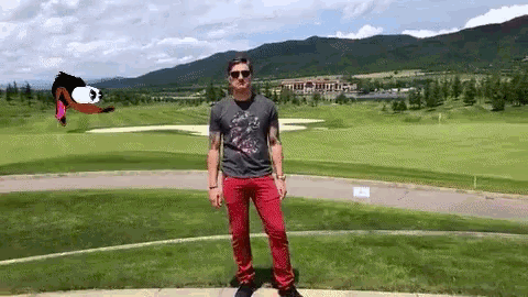 a man in a gray shirt and red pants is standing on a golf course