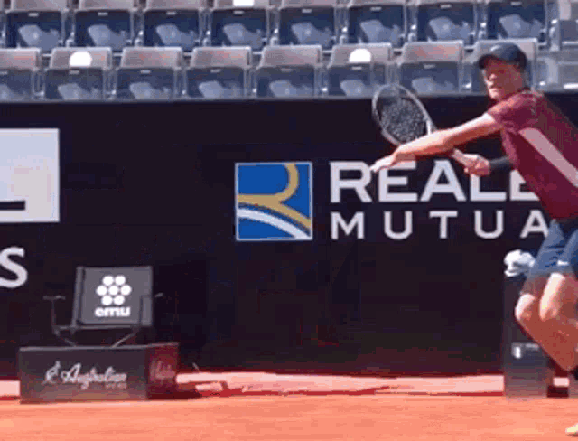 a man swings a tennis racquet in front of a sign that says real mutua