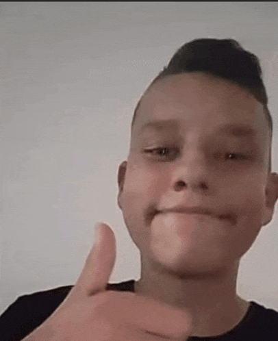 a young boy is giving a thumbs up sign while making a funny face .