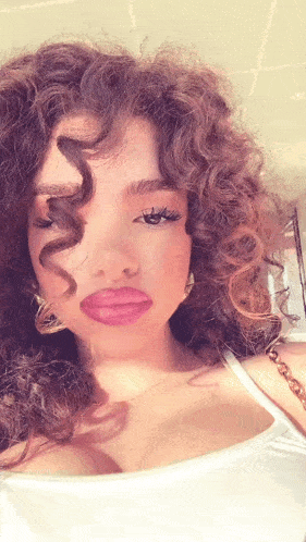 a woman with curly hair is wearing a white tank top and earrings