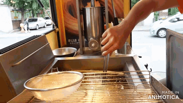 a person is frying food in a fryer with the words made in animotica visible