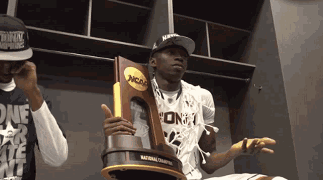 a man is holding a ncaa trophy in a locker room