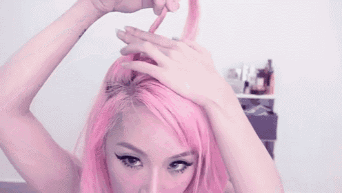 a woman with pink hair is tying her hair in a knot .