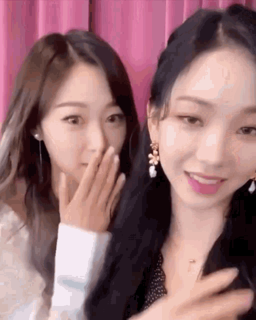 two young women are sitting next to each other and one is covering her mouth with her hand .