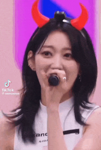 a woman wearing devil horns is holding a microphone .