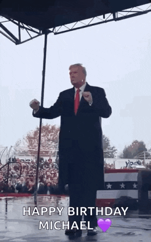 a man in a suit and tie is standing on a stage in front of a crowd and giving a speech .