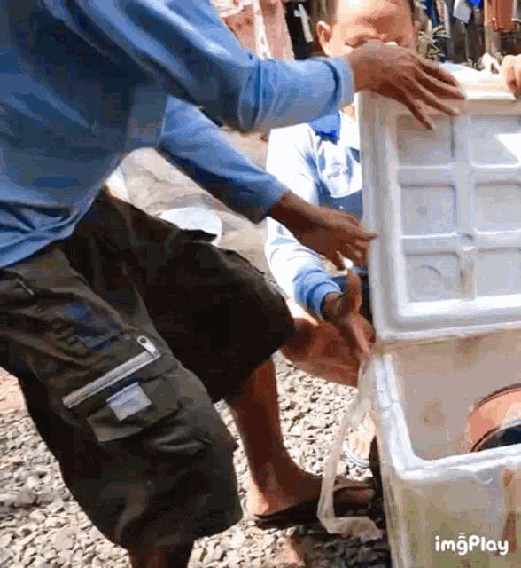 a man in a blue shirt is opening a styrofoam box while another man looks on