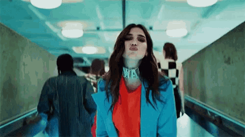 a woman in a blue jacket is blowing a kiss while walking down a hallway with other people .