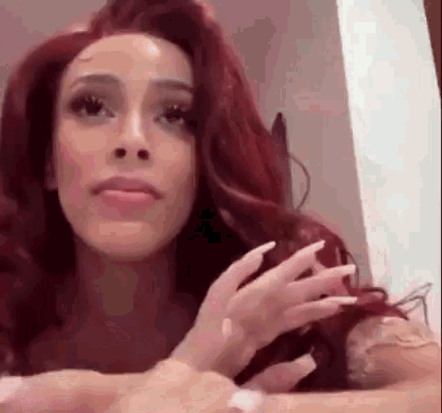 a woman with long red hair and white nails is sitting at a table with her hands in her hair .
