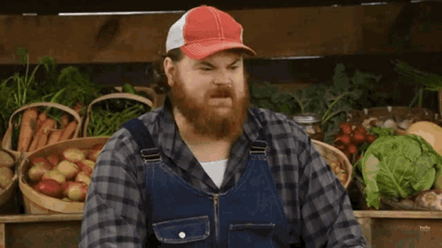 a man with a beard wearing overalls and a red hat stands in front of a sign that says must