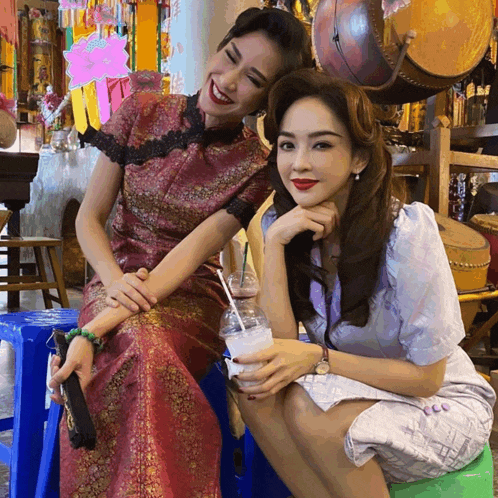 a woman in a red dress sits next to another woman in a blue stool