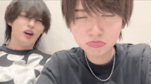 two young men are making funny faces with their eyes closed and one has a chain around his neck