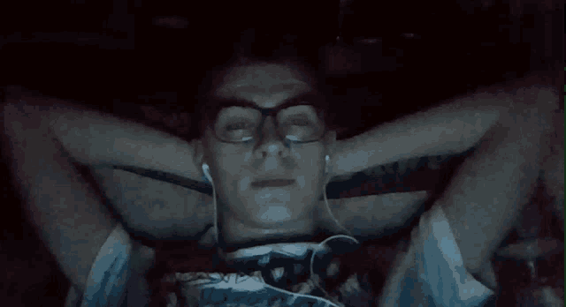 a man wearing glasses and headphones is laying down with his hands behind his head
