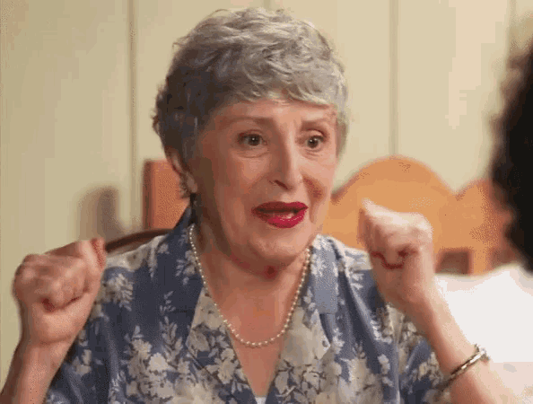 an elderly woman wearing a pearl necklace and a blue floral shirt