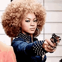 a woman with a big afro is pointing a gun at the camera .