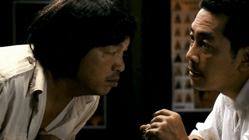 two men are looking at each other in a dark room with a poster in the background .
