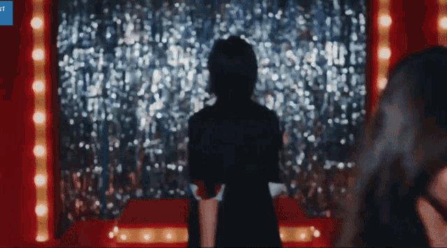 a woman in a black dress stands in front of a red curtain with lights on it