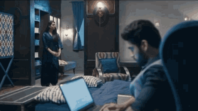 a man is typing on a laptop in a room with a woman standing in the background