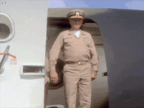 a man in a military uniform stands in front of an airplane door