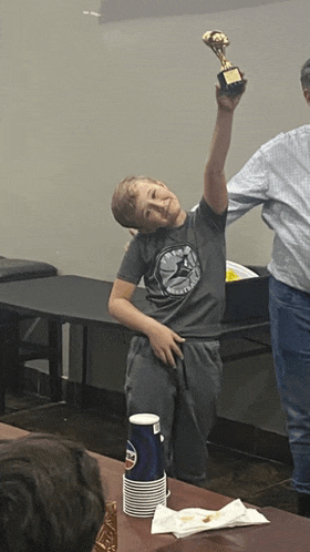 a young boy holds up a trophy while wearing a gray shirt with a basketball on it