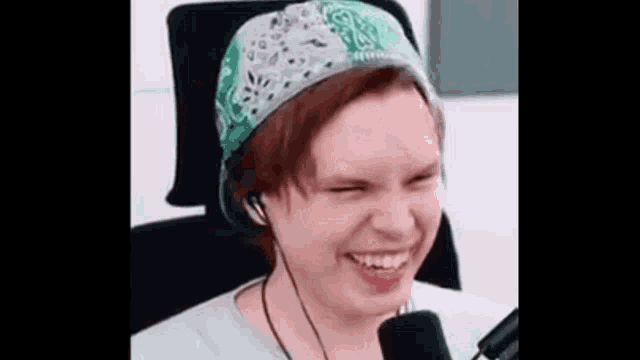 a woman wearing a bandana and headphones is laughing in front of a microphone .