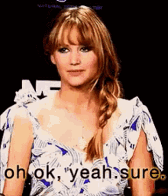 a woman in a blue and white dress is sitting in front of a sign that says `` oh ok , yeah sure '' .