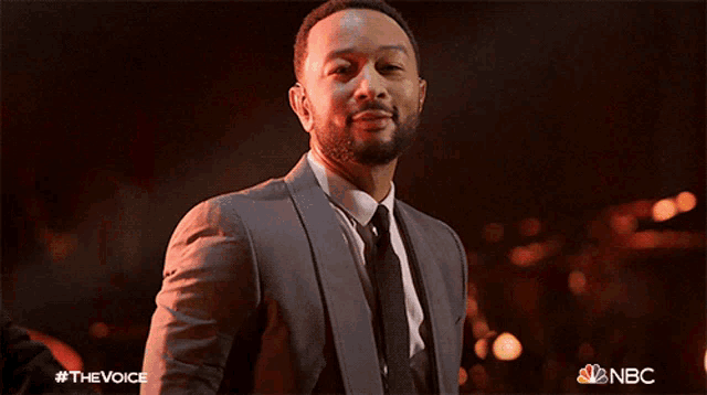 a man in a suit and tie is standing in front of a nbc ad