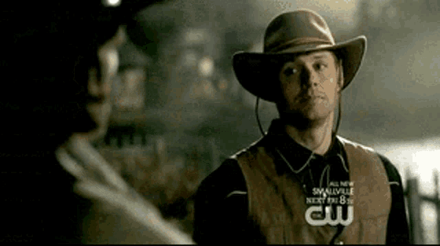 a man wearing a cowboy hat and a vest that says smallville next to him