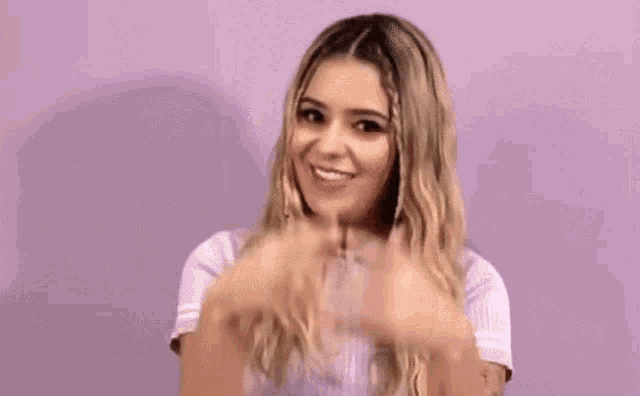 a woman is smiling and touching her head against a purple background .