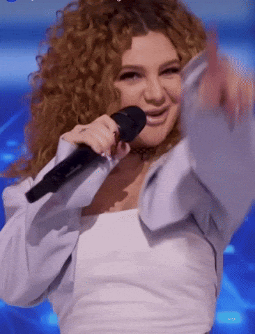 a woman with curly hair is singing into a microphone while wearing a white shirt