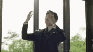 a man in a suit and tie is standing in front of a window covering his eyes .