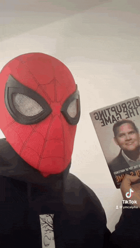 a man wearing a spiderman mask holds a book