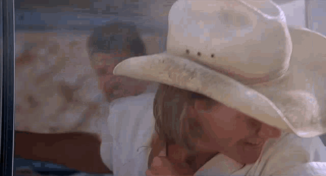 a woman wearing a cowboy hat is talking on a cell phone while a man looks on .
