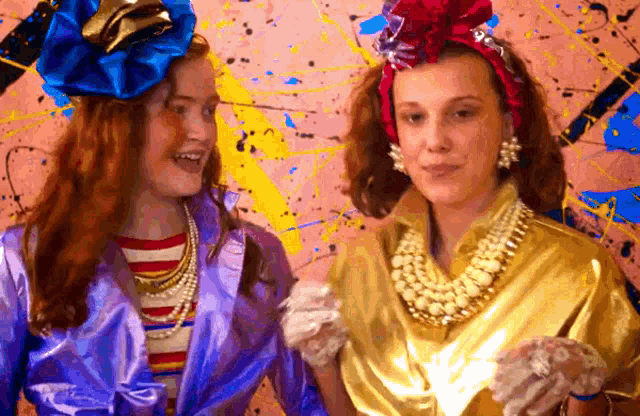 two women are standing next to each other in front of a pink wall .