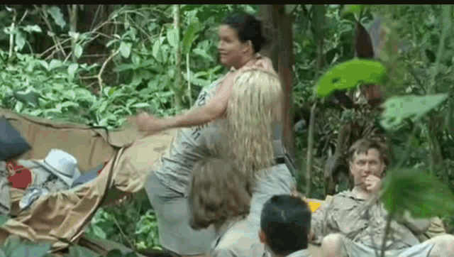 a group of people are sitting in the woods and one woman is carrying another woman on her back .