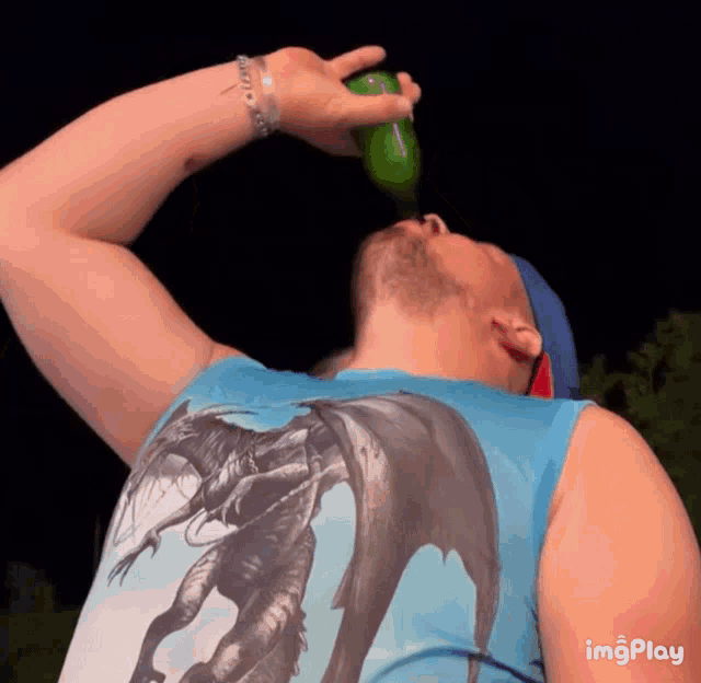 a man in a blue tank top with a dragon on it drinks from a bottle